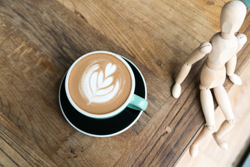 Hot mocha coffee or capuchino in the green cup with a wood man sitting on the wooden table