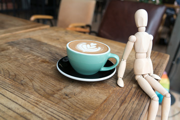 Hot mocha coffee or capuchino in the green cup with a wood man sitting on the wooden table