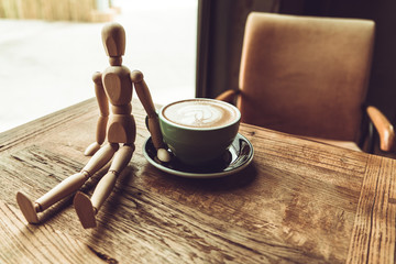 a wood man sitting and touch the hot mocha coffee or capuchino in the green cup on the wooden table