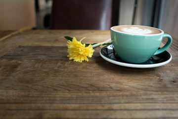 Hot mocha coffee or capuchino in the green cup with heart pattern and yellow flower on the wooden table