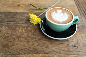 Hot mocha coffee or capuchino in the green cup with heart pattern and yellow flower on the wooden table
