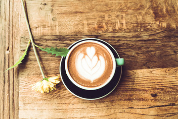 Hot mocha coffee or capuchino in the green cup with heart pattern and yellow flower on the wooden...