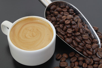 Cup of espresso coffee with metallic shovel and roasted coffee beans on table