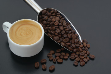 Cup of espresso coffee with metallic shovel and roasted coffee beans on table