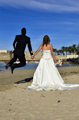 Fototapeta na wymiar Pareja de recién casados saltando en la playa.
