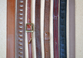 Fashion background. Vintage brown leather belts on a beige cardboard surface closeup.
