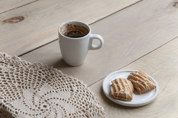 Cozy home still life. A cup of coffee and plate with cookies on knitted napkin on light wooden background. Close up.