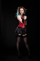 Gorgeous woman in fetish red leather corset on black background in studio photo. BDSM and dominatrix