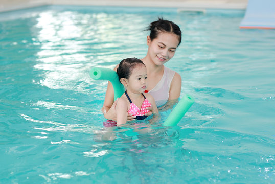 happy smiling asian little girl with mother swimming at water pool.