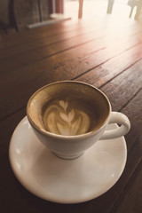 A cup of cappuccino coffee on wooden table in coffee shop background with vintage filter