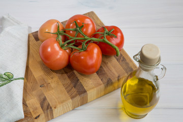 Olive oil and a branch of tomatoes on a white colored wooden background