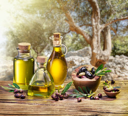 Olive berries in the wooden bowl and bottles of olive oil on the table.