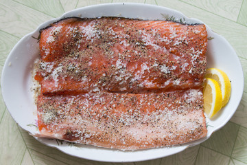 Salting raw salmon fish with  lemon, pepper, sea salt. Top view.