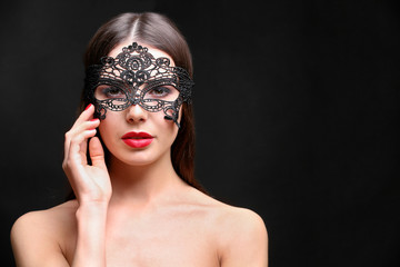 Beautiful young woman in mask on black background