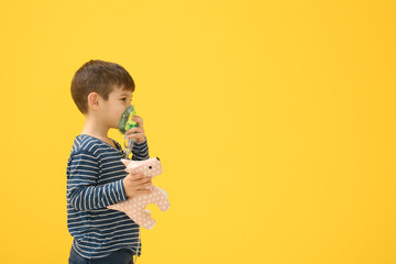 Cute little boy using nebulizer on color background. Allergy concept