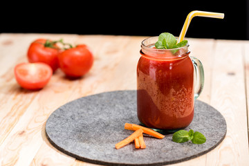 selective focus of fresh tomato smoothie with basil leaves, carrot slices and straw on tabletop