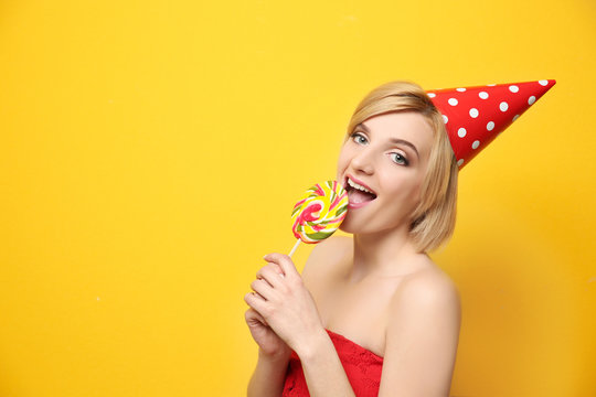 Beautiful woman in party cap holding lollipop on yellow background