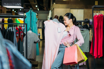 asian hipster girl holding dress and shopping bags in boutique, clothes shopping concept
