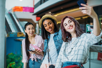 Smiling young women taking selfie in shopping mall, young girls shopping concept