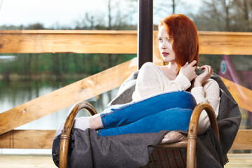 Atractive red-haired woman resting sitting on Rocking chair in f