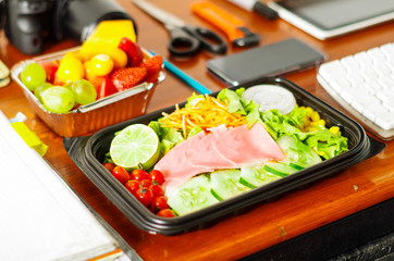 Delicious mediterranean-Style fresh salad with ham and fruit sal in a plastic box on wooden table