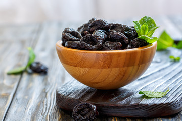 Dried black plums and mint in a wooden bowl. - obrazy, fototapety, plakaty