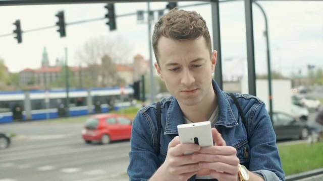 Stylish boy texting messages on smartphone and smiling to the camera, steadycam shot
