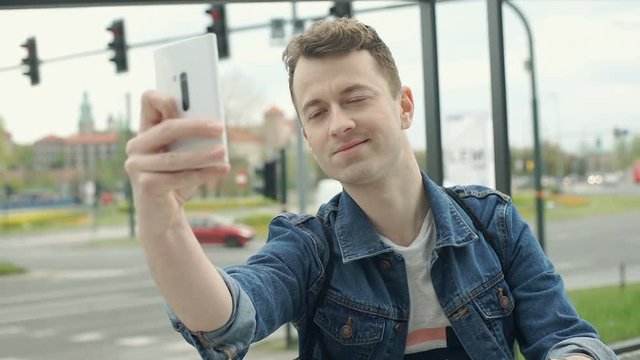 Happy man doing selfies on smartphone in the city, steadycam shot
