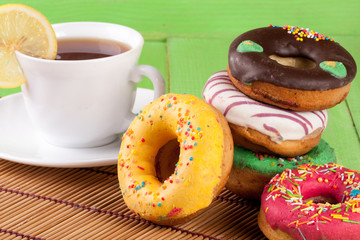 pile of glazed donuts with a cup of tea on a green wooden background