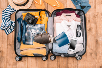 Overhead view of traveler's accessories organized in open luggage on wooden floor