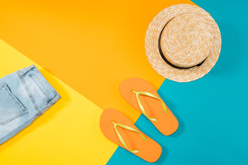 Summer vacation background with orange flip flops, denim trousers and hat on colored copy space