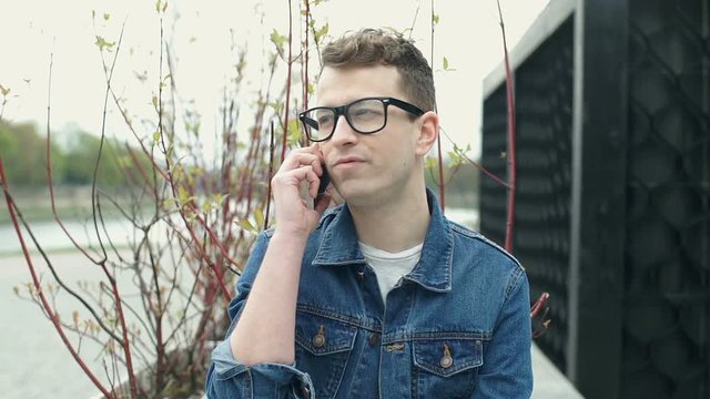 Young man in glasses chatting on cellphone and smiling to the camera, steadycam shot
