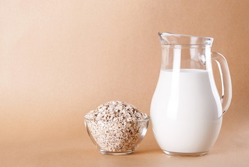 Raw oatmeal in a bowl and milk in a jar on a beige background