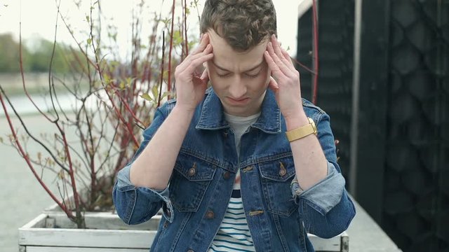 Young man looks worried while having painful headache, steadycam shot
