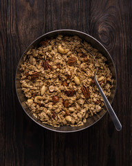 Large bowl of granola with spoon on dark brown wooden background