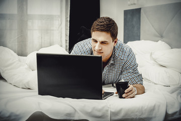 Casual young man using laptop in bed at home.
