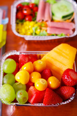 Close up of a delicious fruit salad and blurred mediterranean-Style fresh salad with hamon on aluminium box on wooden table