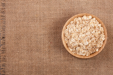 Oat flakes in a wooden bowl on sackcloth with copy space for your text. Top view