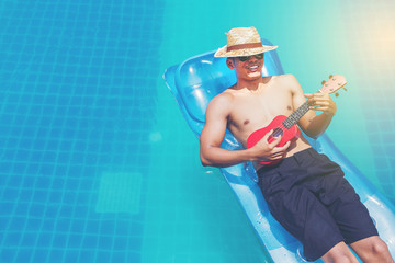 man with ukulele relaxing on the air mattress in the swimming pool. vacation and free time