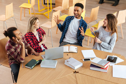 Happy Students Sitting In Library Talking With Each Other.