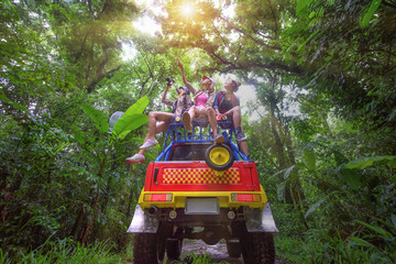 woman in group are enjoy traveling by sitting on the rack-roof of the convertible car off-road in jungle