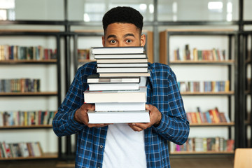 Young afro american male student holding stack of books
