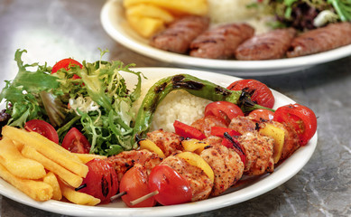 Chicken skewers, french fries and rice with leaf vegetable.