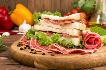 Sandwich with salami. Lettuce, cherry tomatoes, mustard, basil, garlic on wooden background.