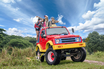 woman in group are enjoy traveling by standing on the rack-back of the convertible car in jungle background