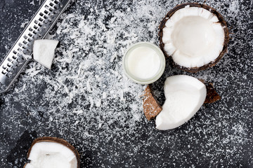 Top view of coconut oil, cracked coconut and shavings with grater on black