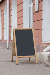 Fototapeta na wymiar An empty chalk board stands on the street. There is a place for an inscription