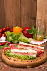 Sandwich with salami. Lettuce, cherry tomatoes, mustard, basil, garlic on wooden background.