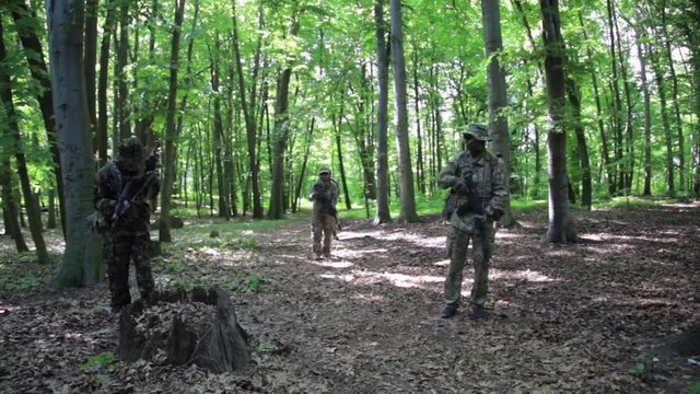 Guerilla warriors squad walking in one formation carrying their guns in the forest bushes.