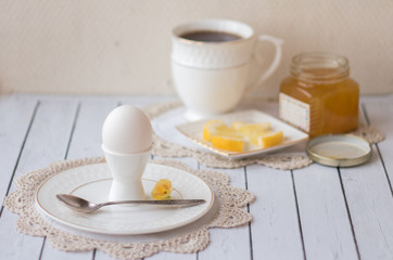 Fototapeta na wymiar Beautiful Breakfast. Boiled egg white on a white stand for the eggs on a white plate on lace crochet doily. Tea in a white Cup, slices of lemon on a saucer, homemade lemon jam. A warm light.